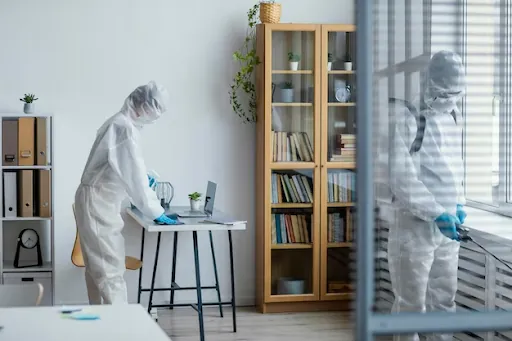 Two workers in protective suits disinfecting a living room