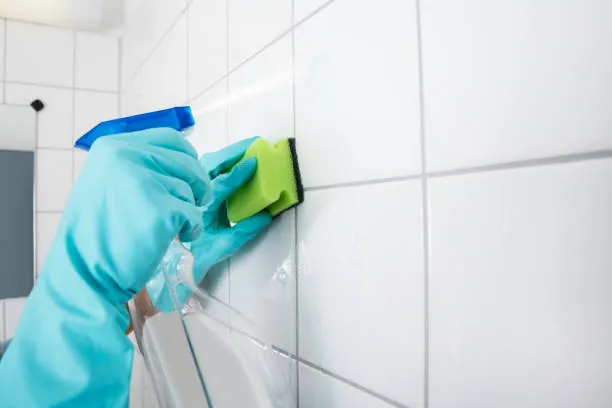 Gloved hand scrubbing white wall tiles with a sponge