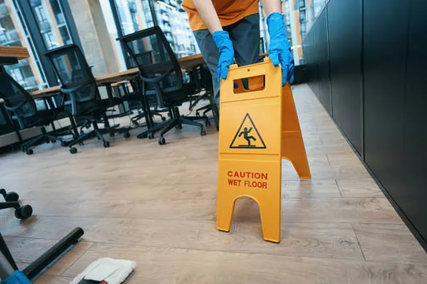 Cleaner placing a caution wet floor sign in an office