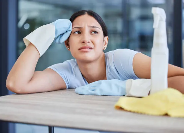 Tired cleaner resting her head on a table beside a cloth and spray