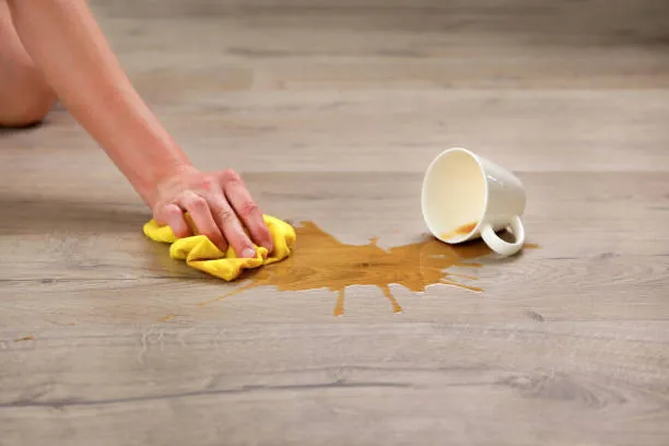 Gloved hand wiping up a spilled cup of coffee from a wooden floor