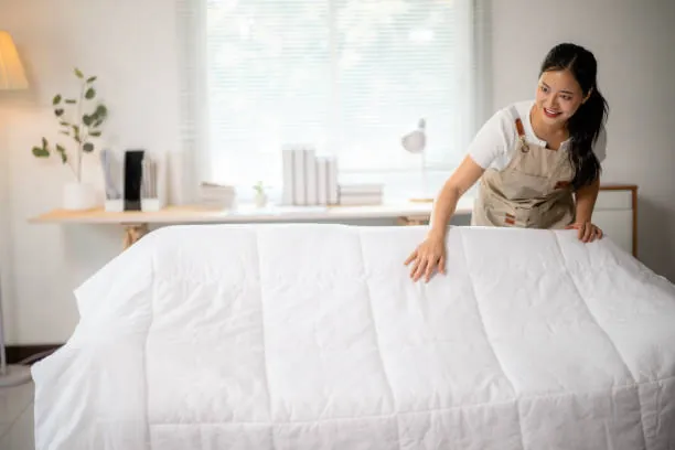 Woman smoothing a white duvet over a bed