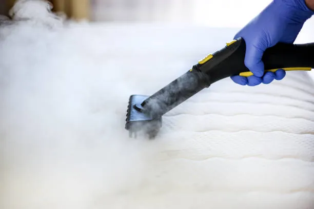 Gloved hand steam cleaning a mattress surface
