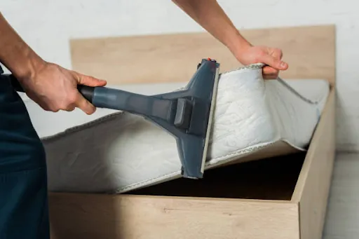 Hands vacuuming the side of a mattress with an upholstery tool