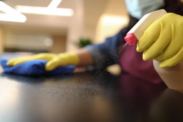 Gloved hands spraying and wiping a wooden surface