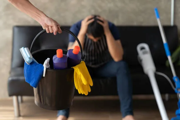 Man sitting with his head in his hands beside a bucket of cleaning supplies