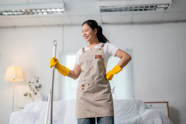 Cleaner holding a mop in a tidy bedroom