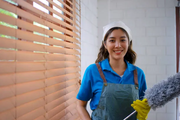 Cleaner with a duster in front of wooden window blinds