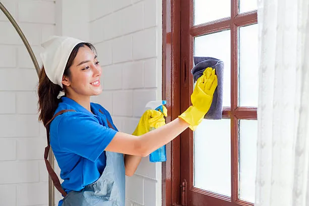 Cleaner wiping a window frame with a cloth and spray