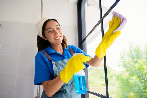 Cleaner wiping a window with a cloth and spray bottle